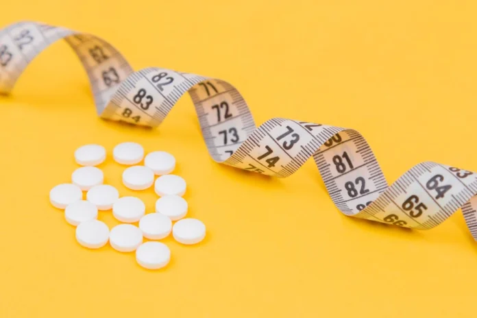 best bipolar medication for weight loss - White measuring tape with a white pills, white vitamin on a yellow background. Diet. Slimming. Obesity. Place for an inscription. Weight loss marathon. Advertising. Top view. The close plan.